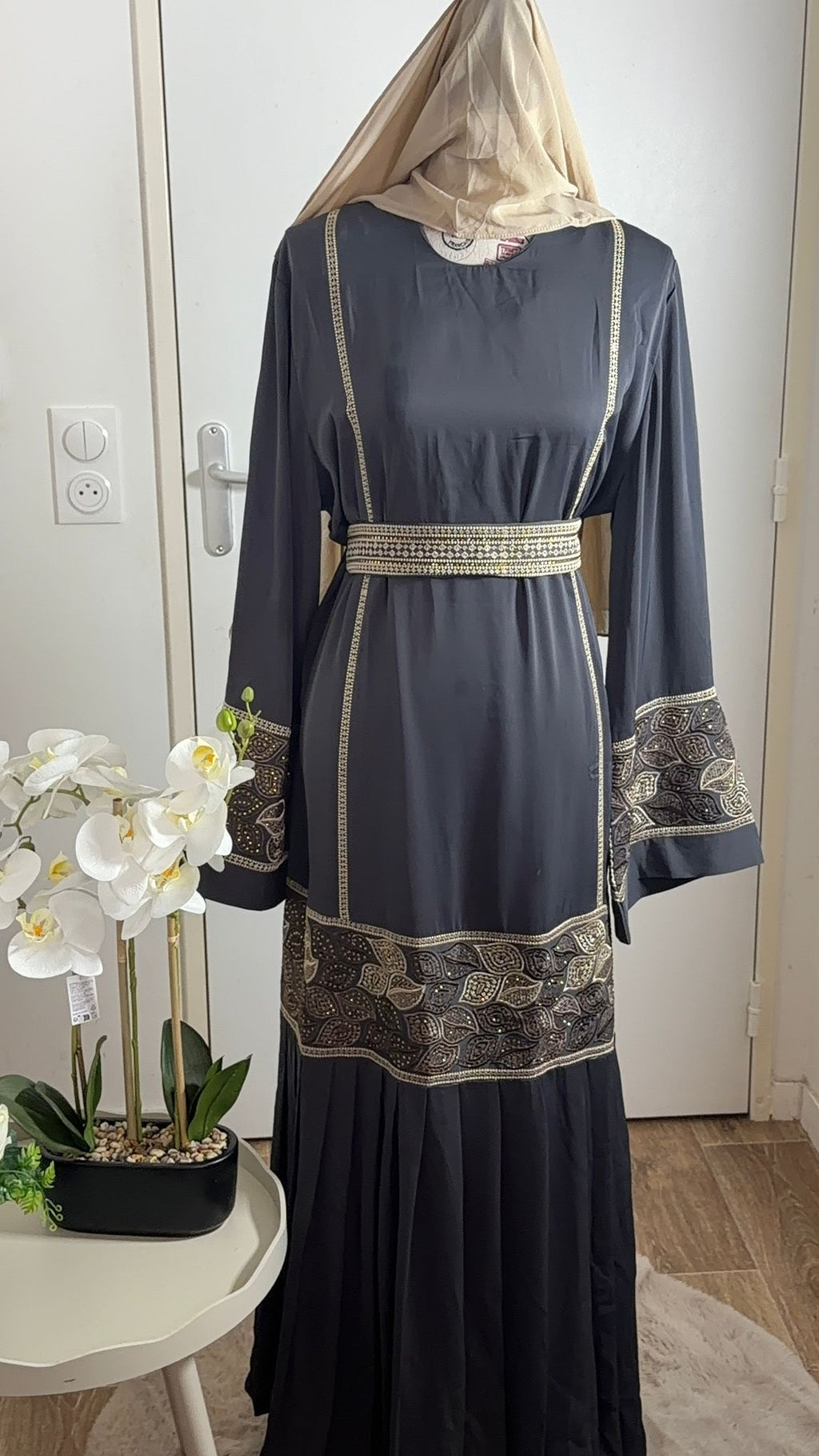 Elegant dark grey abaya with gold embroidered cuffs and waist belt, paired with a beige hijab.