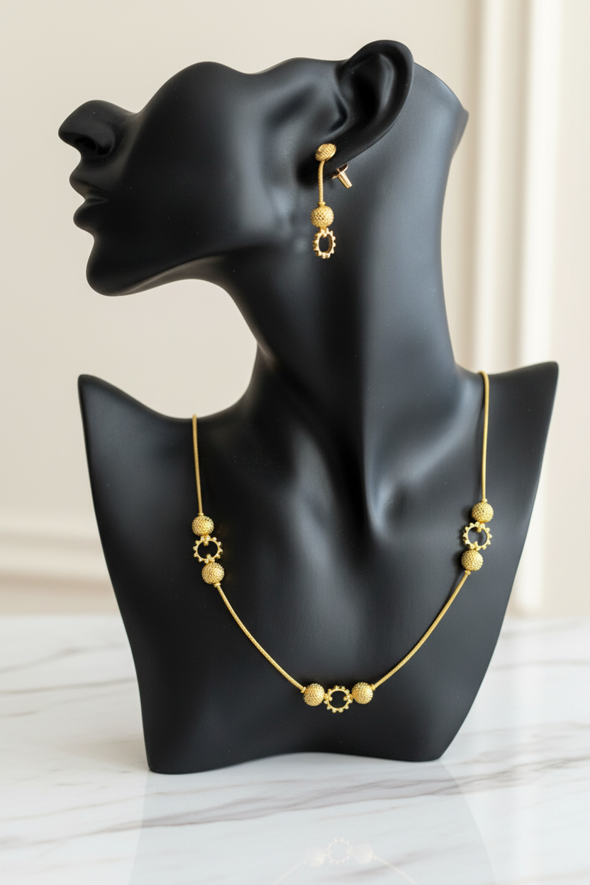 Parure collier et boucles d'oreilles motif boule plaquée or, présentée sur buste mannequin noir