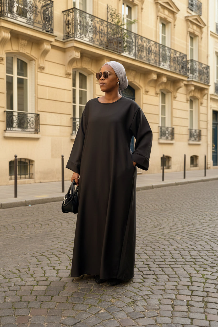 Abaya Mina noire – vue de face, rue pavée en arrière-plan