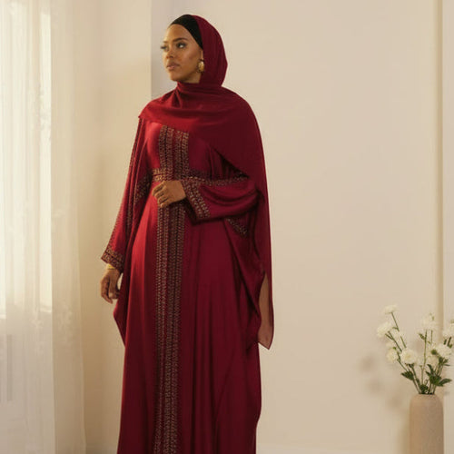 Elegant deep red flowing abaya with intricate gold embroidery on front and sleeves, draped loose fit with matching headscarf.