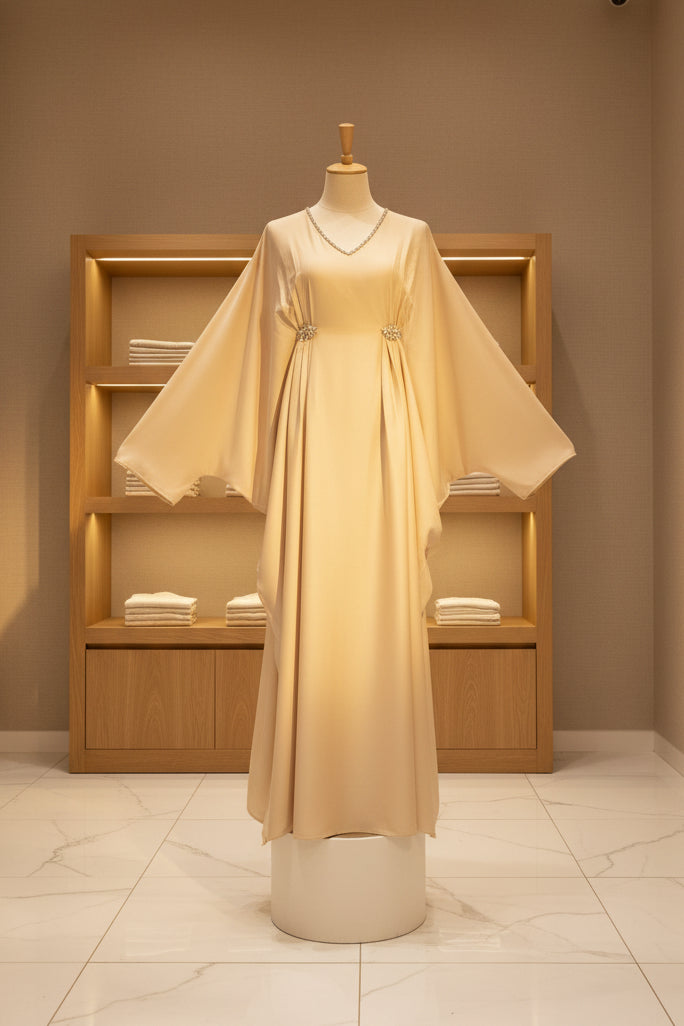 Cream-colored flowing abaya with wide bishop sleeves and V-neck on mannequin in minimalistic setting.