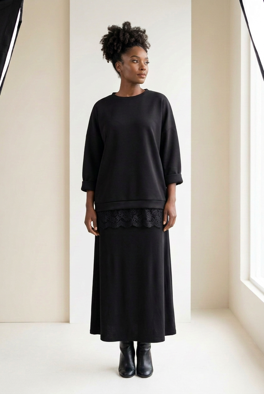 Pull long oversize Aicha noir porté avec une jupe longue noire, bas en dentelle qui dépasse